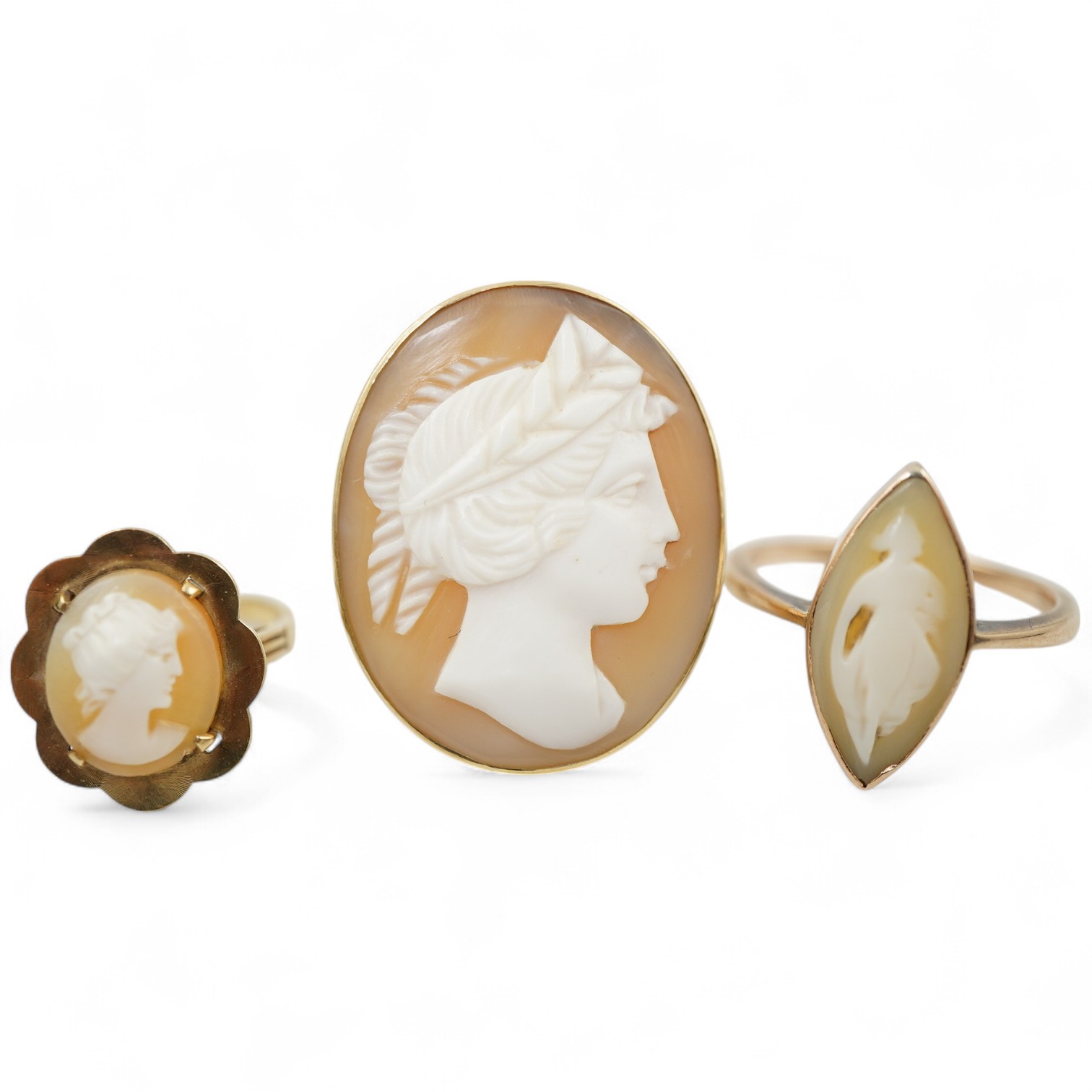 A group of three shell cameo rings, two depicting a classical lady in profile, one of navette-shaped outline depicting a dancing figure, each mounted in gold, two stamped 9ct, largest size V, largest cameo 3 x 2.4cm, com